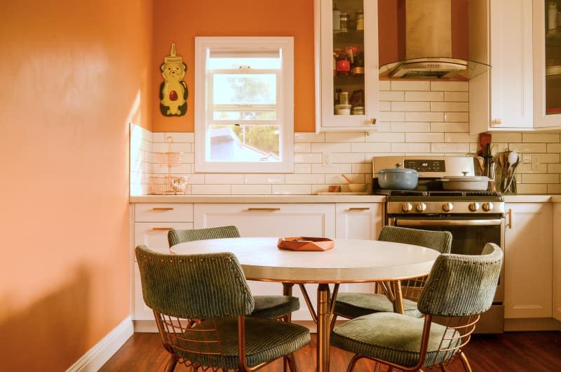Round table and chairs anchor orange kitchen with white tiles.