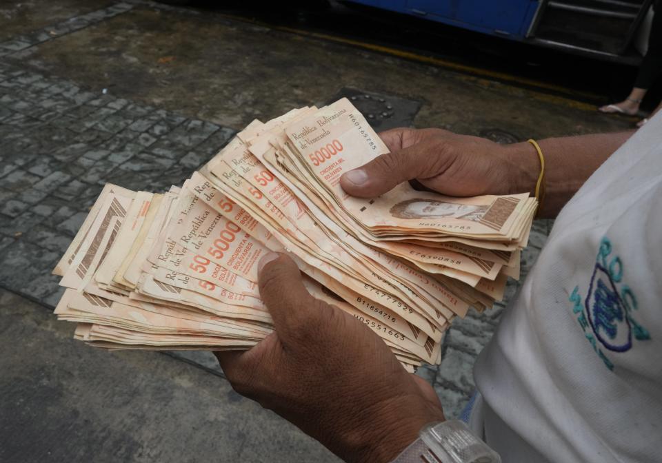 FILE - In this Aug. 5, 2021 file photo, a man counts Bolivar bills that amount to $1, at a bus stop in Caracas, Venezuela. A new currency with six fewer zeros debuts Friday, Oct. 1, 2021, in Venezuela, whose currency has been made nearly worthless by years of the world's worst inflation. (AP Photo/Ariana Cubillos,File)