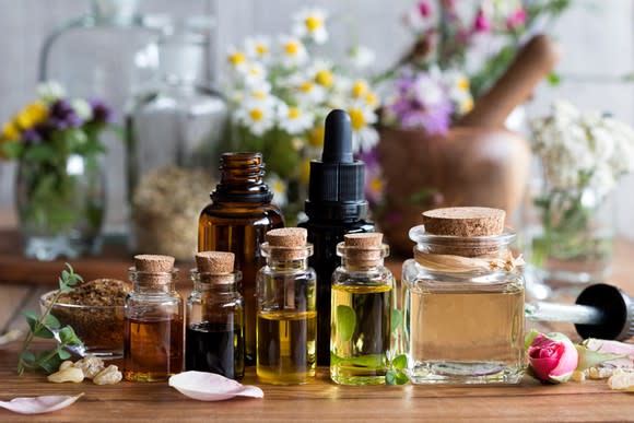 Bottles of varying sizes of essential oils sitting on a table, with vases of flowers in the background