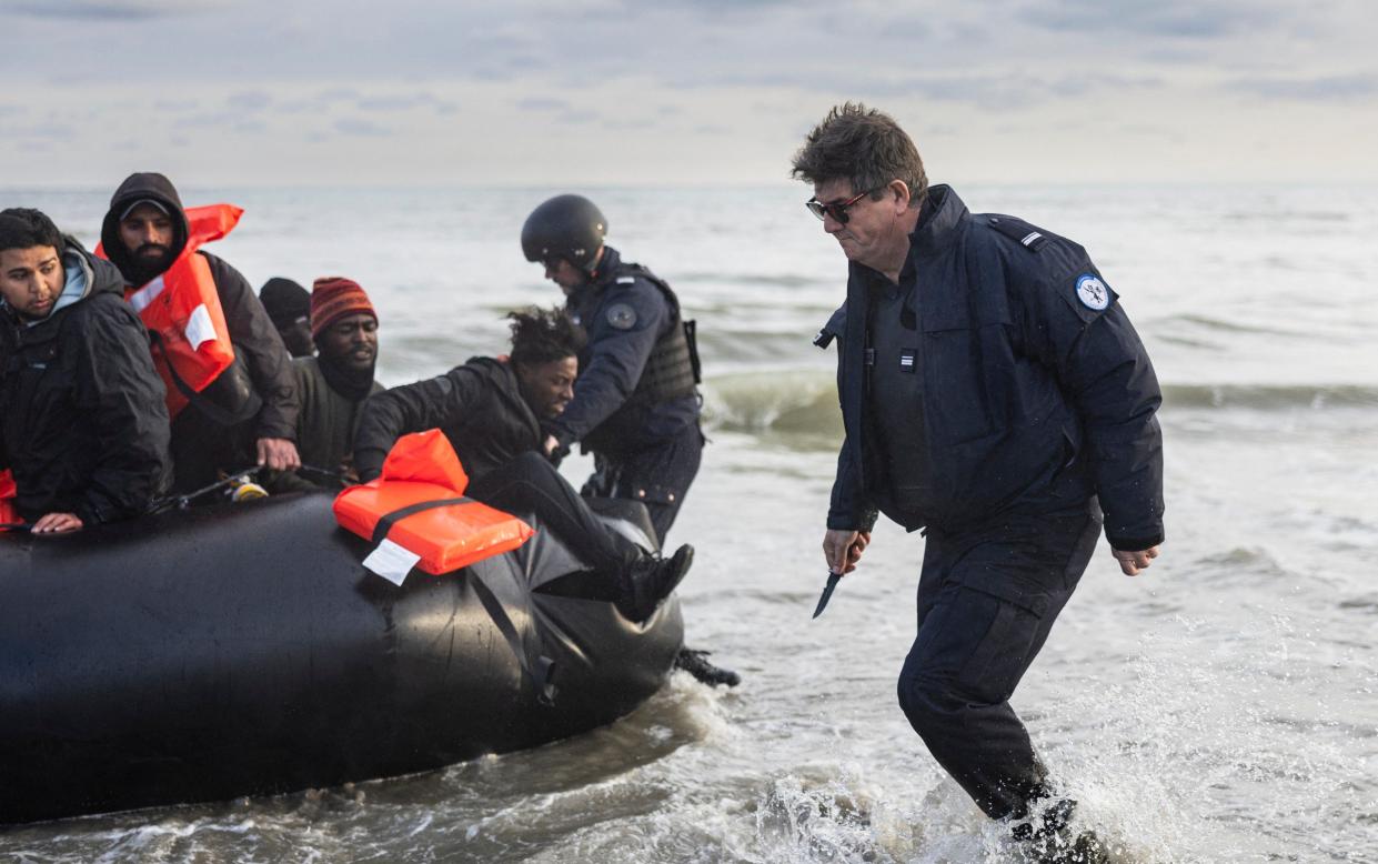 French police officers puncture a smuggler's boat with a knife to prevent migrants from embarking in an attempt to cross the English Channel