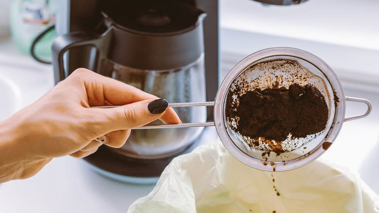 Hand dumping ground basket of coffee maker