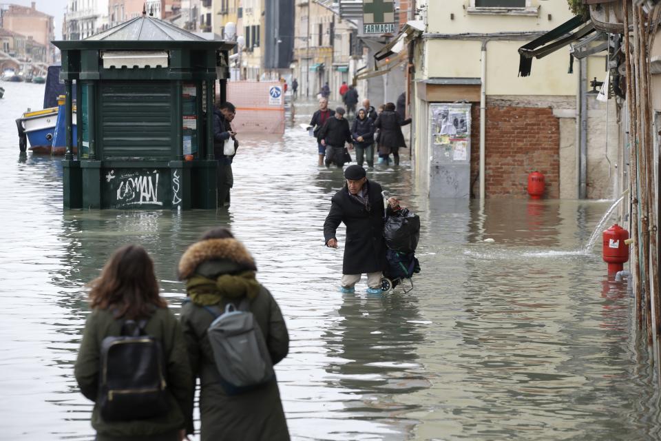 People wade through water during a high tide, in Venice, Wednesday, Nov. 13, 2019. The high-water mark hit 187 centimeters (74 inches) late Tuesday, Nov. 12, 2019, meaning more than 85% of the city was flooded. The highest level ever recorded was 194 centimeters (76 inches) during infamous flooding in 1966. (AP Photo/Luca Bruno)