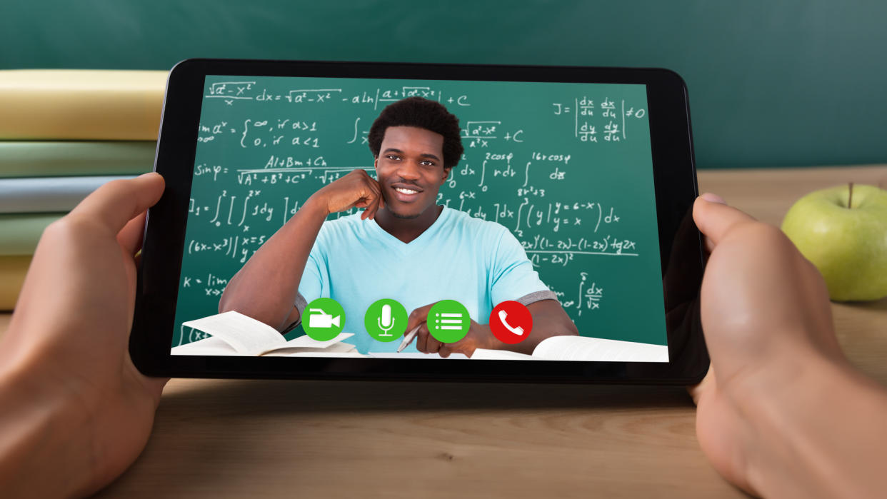 Close-up Of A Student's Hand Video Conferencing With Happy Male Teacher On Digital Tablet.