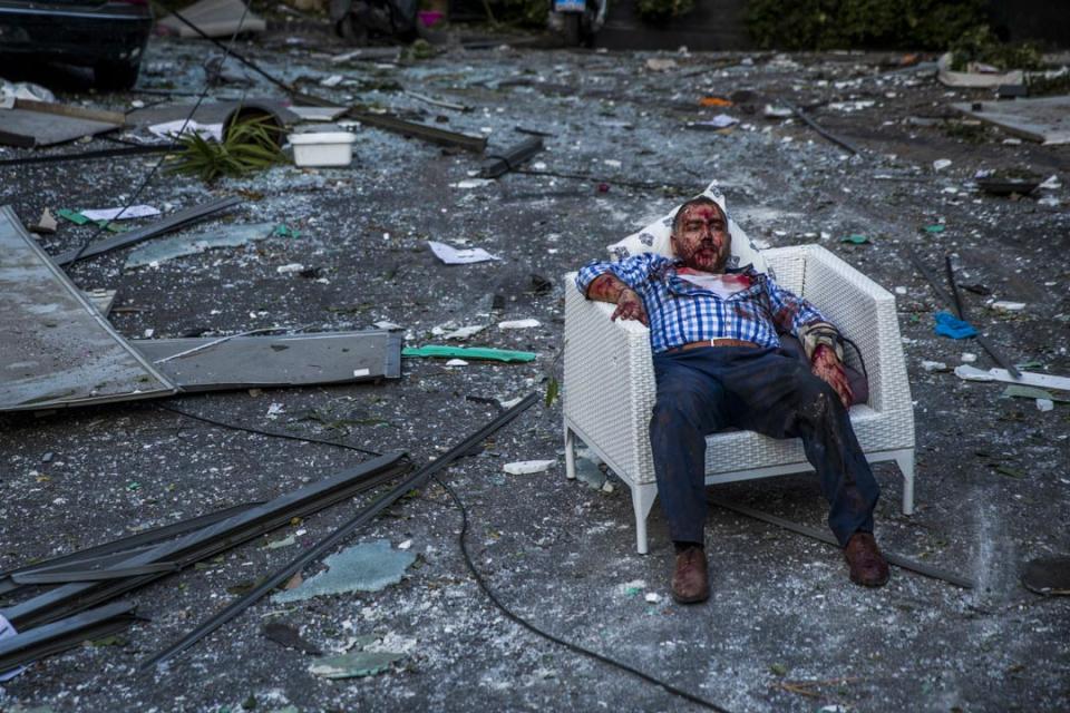 一名受傷男子在爆炸現場遺下的椅子上坐下休息。