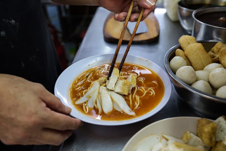 Various toppings like flour fritters, fishcake slices and fried beancurd are added to the noodles.