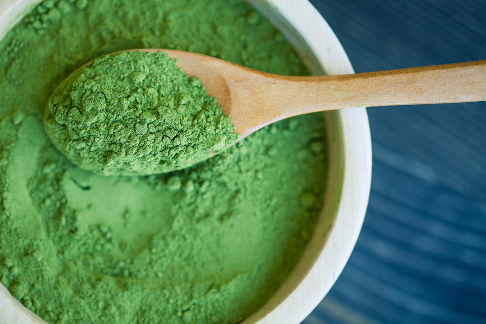 Green powder in a container being scooped with a wooden spoon.