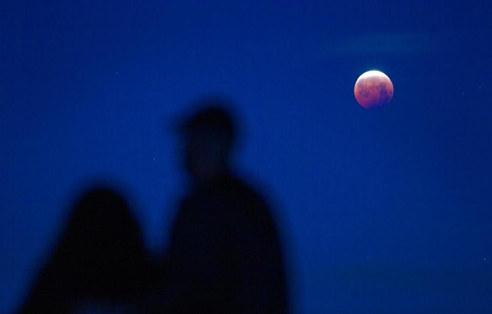 Julie Corrales, left, and Daniel Murray watch the waning "Super Flower Blood Moon" lunar eclipse from Skinner Butte early Wednesday morning. During a lunar eclipse, the moon travels through Earth's shadow. and the light bent through the Earth's atmosphere gives the moon a reddish glow. A "supermoon," an informal term that describes times when the full moon is at perigee, or its closest point to Earth, making it look extra big and bright in the night sky. Photo was taken at ISO 800, 1/8th of a second, at f3.5.