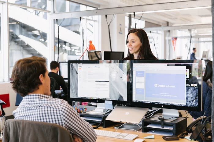 Two workers in an office with Dropbox running across two monitors.