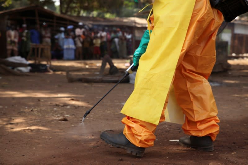 FILE PHOTO: A member of the French Red Cross disinfects the area around a motionless person suspected of carrying the Ebola virus as a crowd gathers in Forecariah