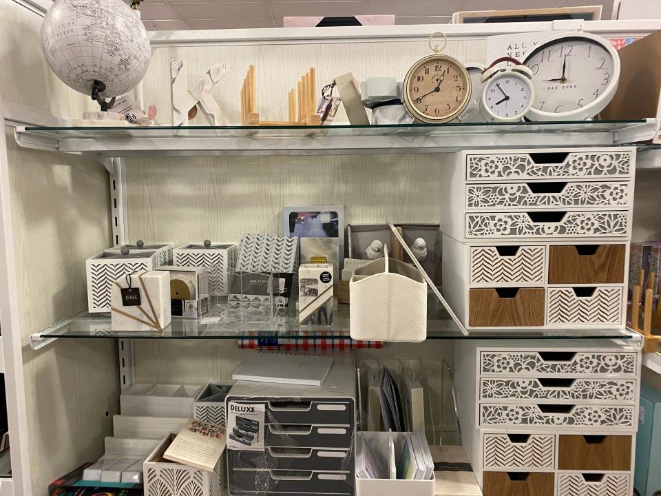 Clocks, paper holders, and small drawer units on glass shelves in a homegoods store