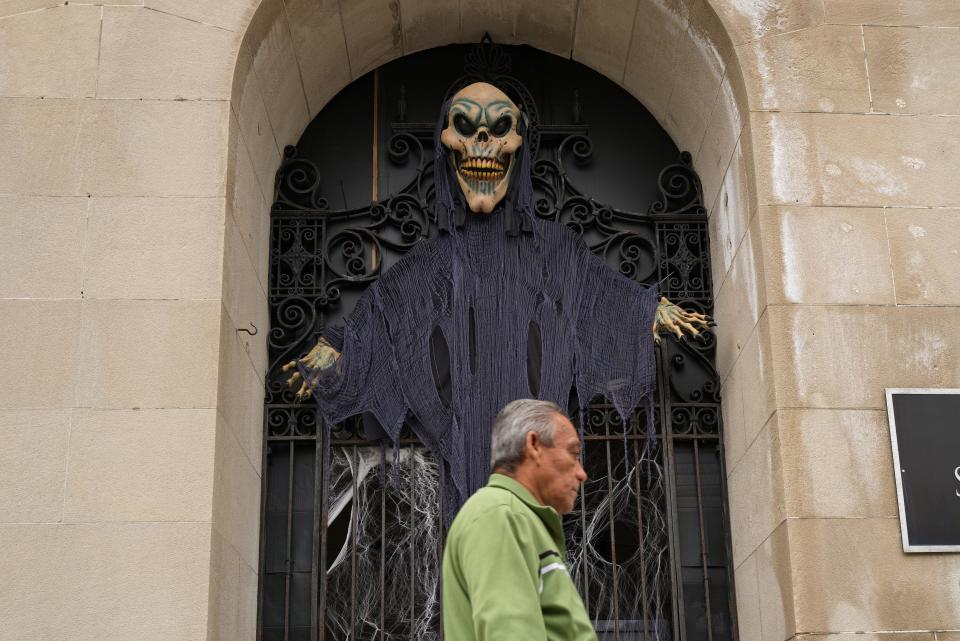 A man passes a Halloween figure installed in front of the Union Square building on Union Street in New Bedford.