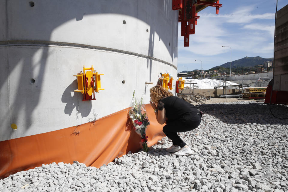 A relative of one of the victims leaves flowers on one of the pillars of the new bridge being built, during a remembrance ceremony to mark the first anniversary of the Morandi bridge collapse, in Genoa, Italy, Wednesday, Aug. 14, 2019. The Morandi bridge was a road viaduct on the A10 motorway in Genoa, that collapsed one year ago killing 43 people. (AP Photo/Antonio Calanni)