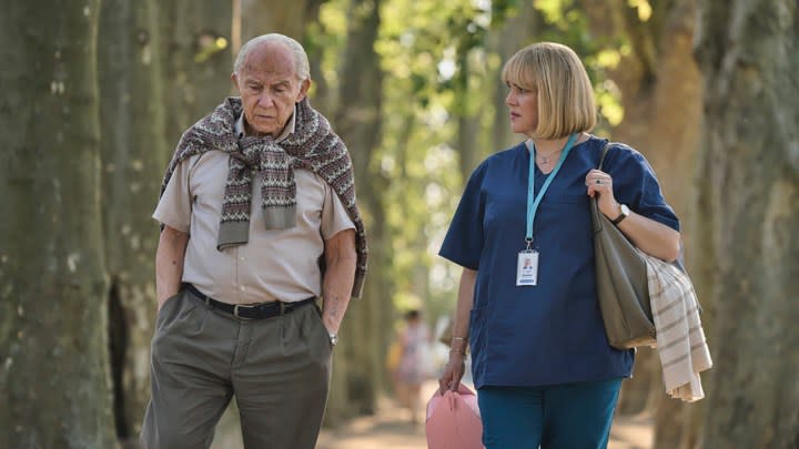 An older man and young woman walk down the street together in a scene from The Tattooist of Auschwitz on Peacock.