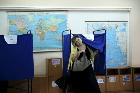 A woman exits a voting booth next to a world map and a map of Greece before voting in a general election at a polling station in Athens, Greece, September 20, 2015. REUTERS/Alkis Konstantinidis