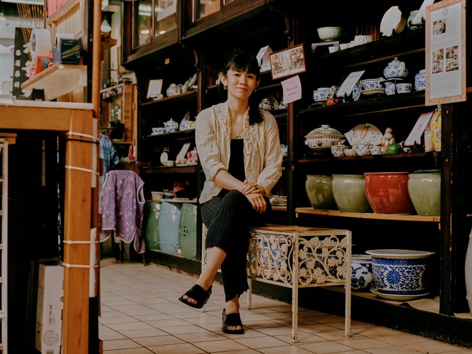 A woman sits on a bench in a shop full of porcelain goods.