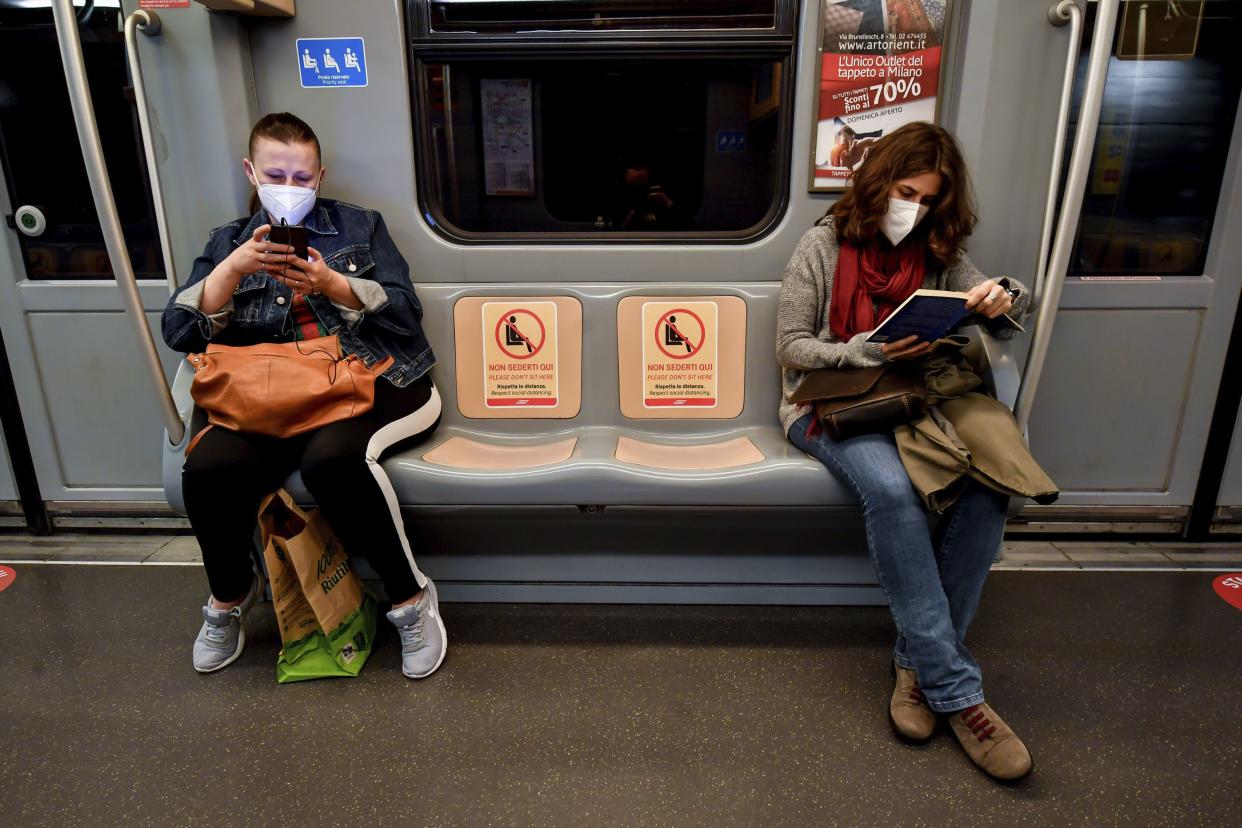 Commuters read a book and check their smartphones in a subway train as signs reading "please do not seat here, respect social distances" are written on seats in Milan, Italy on Monday, April 27, 2020. Italian factories, construction sites and wholesale supply businesses can resume activity as soon as they put safety measures into place aimed at containing contagion with COVID-19. This concession comes with partial easing of national lockdown restrictions announced Sunday night by Italian Premier Giuseppe Conte.