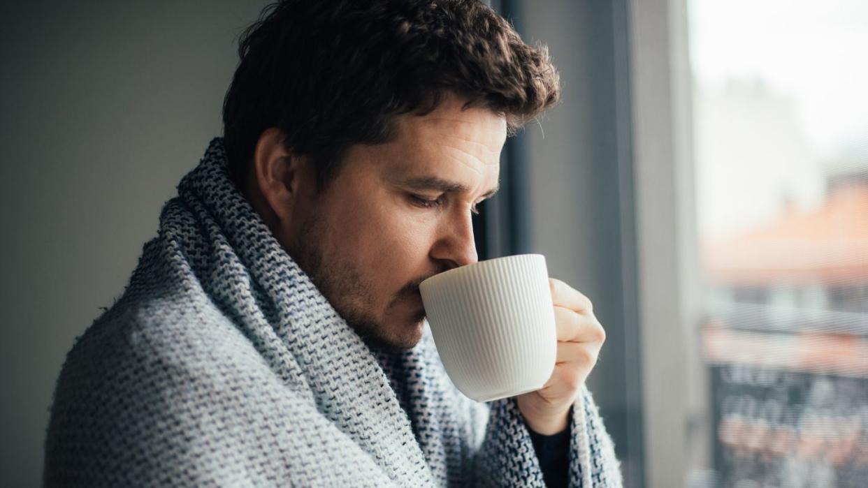 sick man trying to warm up with blanket and a cup of hot beverage