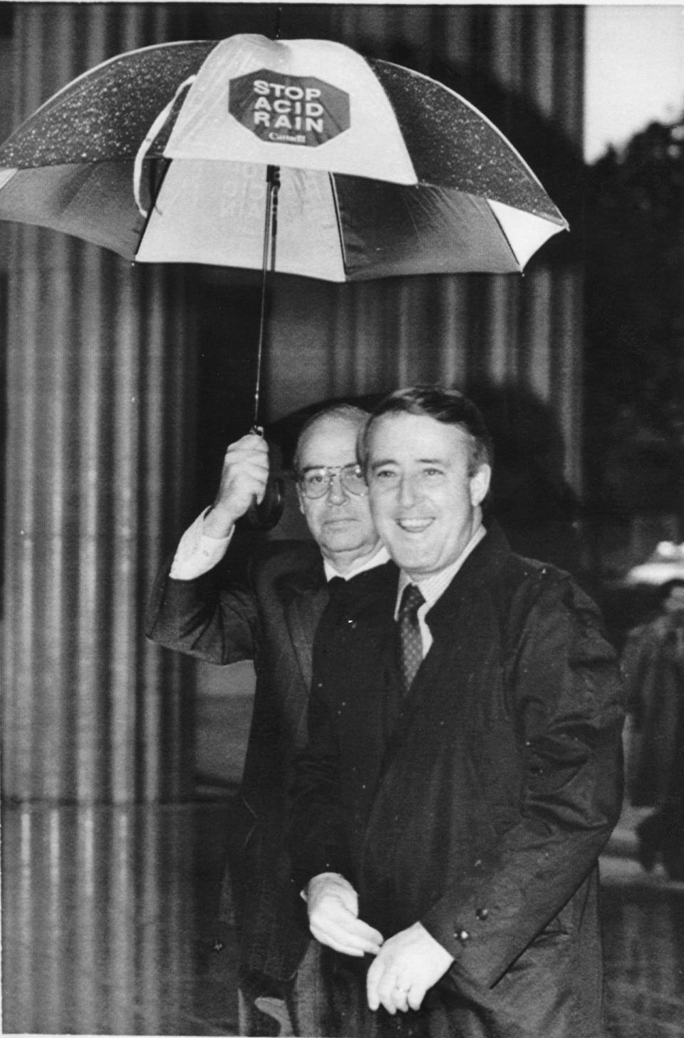 Prime Minister Brian Mulroney arrives in the rain at a Washington television studio Friday morning, May 5, 1989 where he appeared in an interview. Holding the Stop Acid Rain umbrella is Canadian Ambassador to the United States Derek Burney.