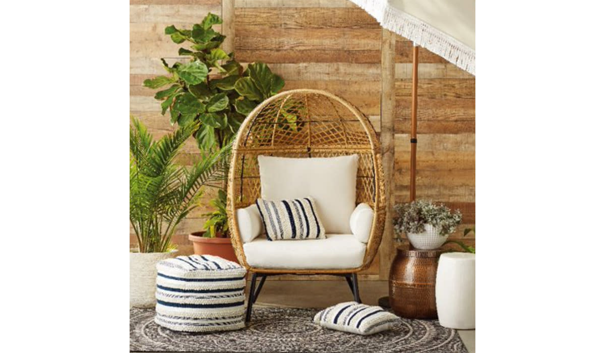 Rattan egg chair with white cushions in a cozy wooden and plant-filled space