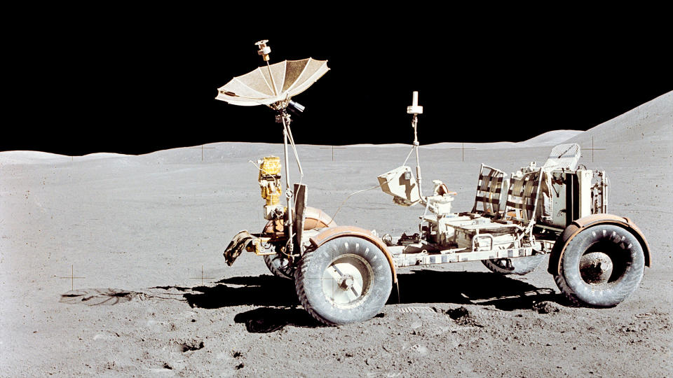 A white, four-wheeled rover sits on the lunar surface