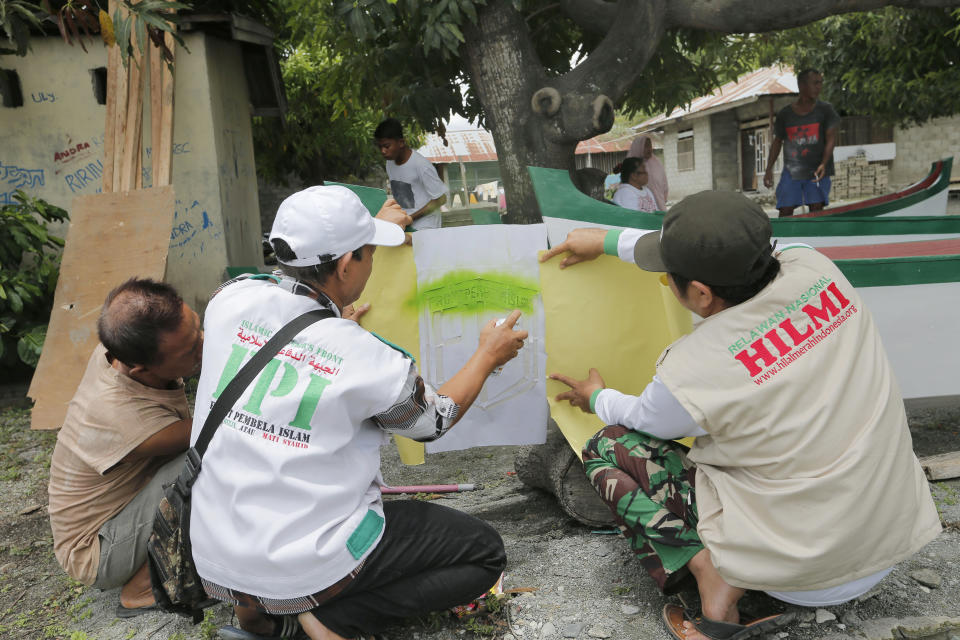 In this April 2, 2019, photo, members of Islamic Defenders Front paint their group's logo as they help local fishermen to build boats at a fishing village affected by the 2018 tsunami in Palu, Central Sulawesi, Indonesia. The Islamic Defenders Front, known for vigilante actions against gays, Christmas decorations and prostitution, has over the past 15 years repurposed its militia into a force that's as adept at searching for earthquake victims as it is at inspiring fear.(AP Photo/Tatan Syuflana)