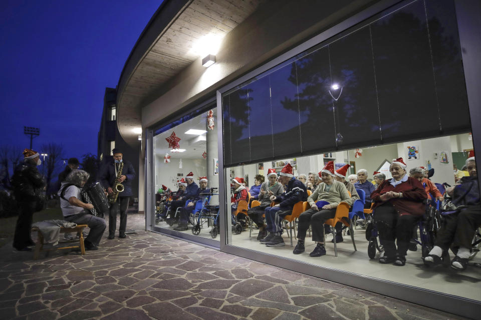Hosts, protected by a glass window, attend a Christmas concert at the Martino Zanchi nursing home in Alzano Lombardo, one of the area that most suffered the first wave of COVID-19, northern Italy, Saturday, Dec. 19, 2020, as the hosts celebrate Christmas. (AP Photo/Luca Bruno)