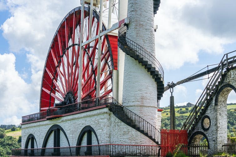 A large red and white wheel next to a tower.