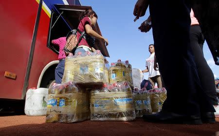 People stand next to cartons of cooking oil while they wait for transportation, after arriving from Brazil, at the bus terminal in Santa Elena de Uairen, Venezuela August 2, 2016. REUTERS/William Urdaneta