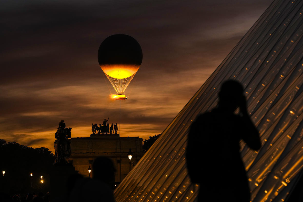 A man takes photos as the Olympic flame rises on a balloon from the courtyard of the Louvre during the Summer Olympics on Sunday.