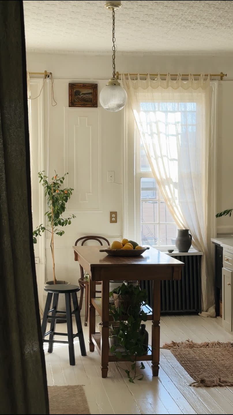 a dining room table with a bowl of fruit on it and long sheers on windows