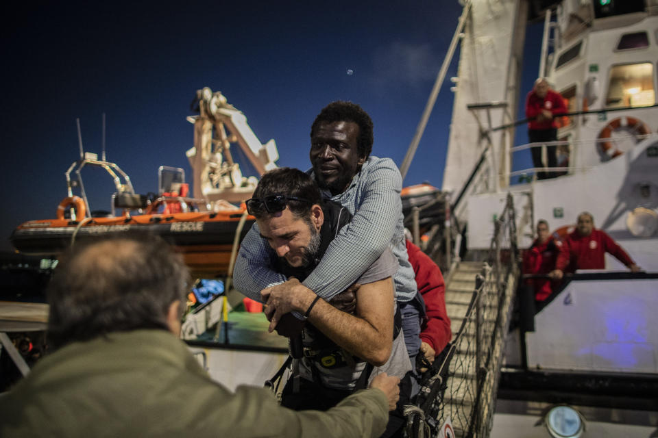 Louis, from Ivory coast, who suffers disability in one leg is helped by David, an aid worker of the Spanish NGO Open Arms, to disembark from the rescue vessel at the port of Messina after being rescued along with other 121 people from different nationalities off the Libyan coast, Sicily, Italy, Wednesday Jan.15, 2020. (AP Photo/Santi Palacios)