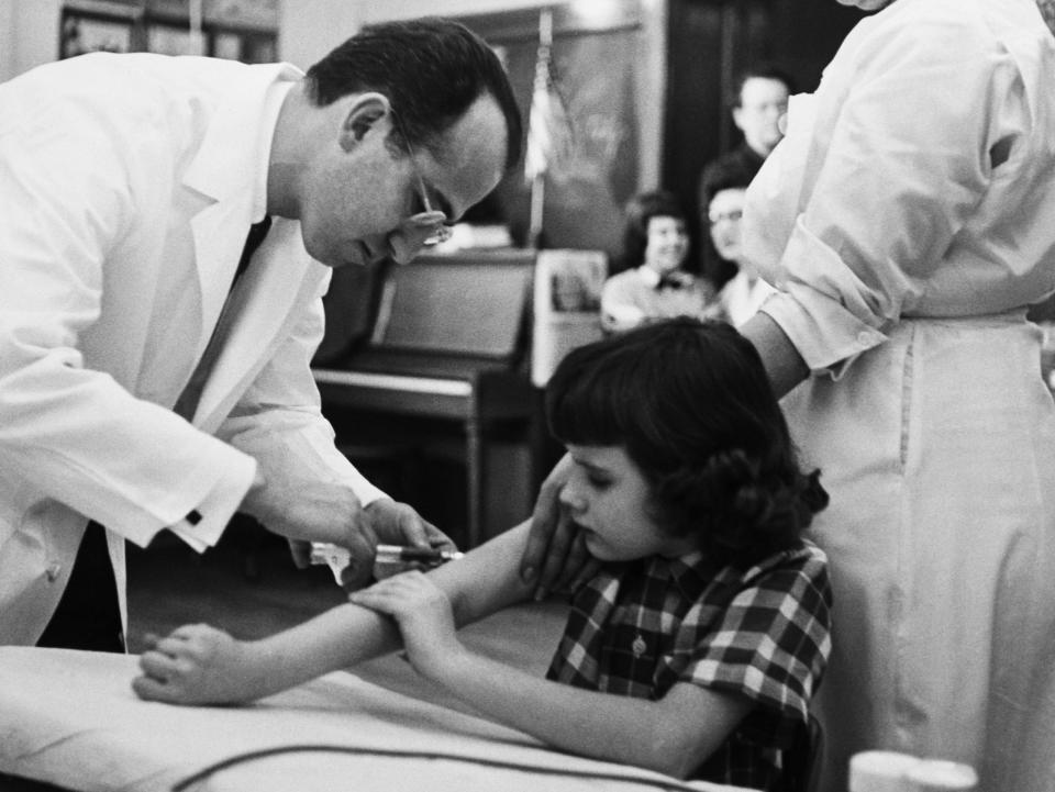 Dr. Jonas Salk gives a shot of the polio vaccine to a girl during test trials.