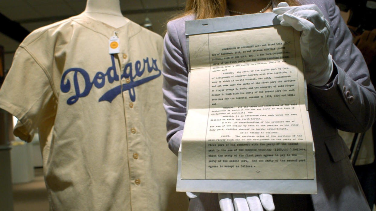 Mandatory Credit: Photo by Justin Lane/EPA/Shutterstock (7832497a)The Hands of a Sotheby's Employee Hold Up the Original 1919 Contract (r) That Traded Baseball Player Babe Ruth From the Boston Red Sox to the New York Yankees Next to Ruth's 1938 Brooklyn Dodgers Uniform (l) During a Preview of a Sports Memorabilia Auction to Take Place 10 June 2005 at Sotheby's Friday 3 June 2005 in New York the Contract Seen Here is Expected to Sell For Over $500 000 (usd) the Uniform For Over $150 000 (usd) and the Money Will Go to a Hunger Relief CharityUsa New York Sports Memorabilia Auction - Jun 2005.