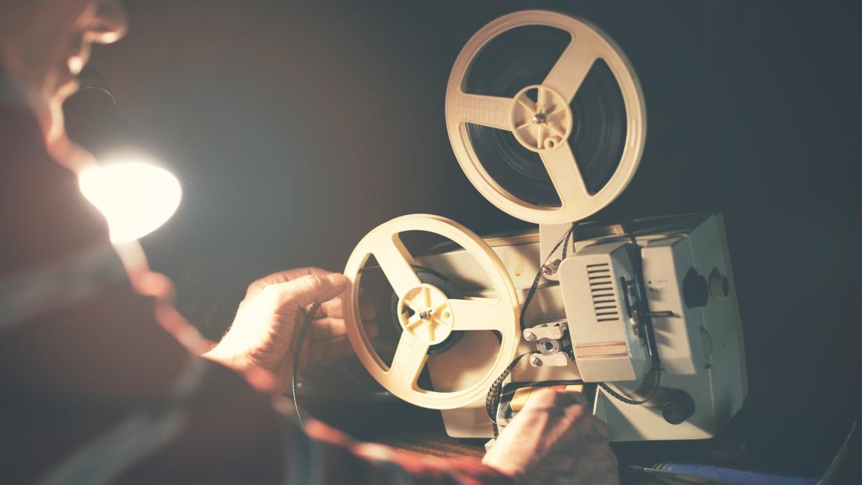 man set up film reel on vintage 8mm movie projector in dark room.