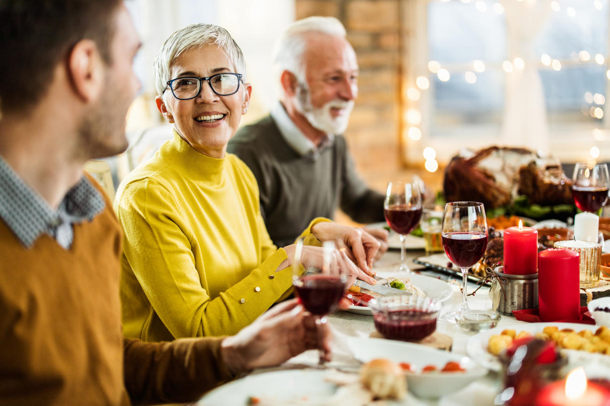 Happy mature woman having Thanksgiving meal with her husband and talking to her adult son at dining table. 