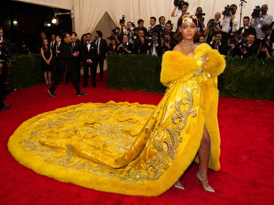 A woman standing on the red carpet with a mustard color dress and gold design.