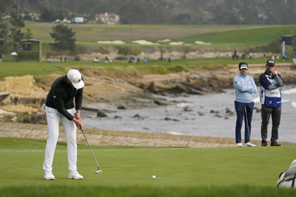 Daniel Berger makes an eagle putt on the 18th green of the Pebble Beach Golf Links during the final round of the AT&T Pebble Beach Pro-Am golf tournament Sunday, Feb. 14, 2021, in Pebble Beach, Calif. Berger won the tournament. Russell Knox, second from right, of Scotland, looks on. (AP Photo/Eric Risberg)