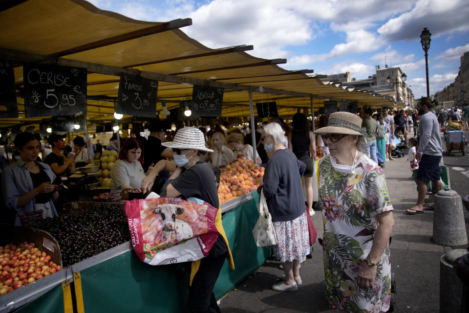 FILE - People shop at a market in Versailles, outside Paris, France, on July 3, 2022. From taxing billionaires and making gasoline cheaper to earlier retirement and higher wages, opposing left-right blocs in France's election are making costly campaign promises that are spooking investors as they seek to woo voters and sideline President Emmanuel Macron. (AP Photo/ Christophe Ena, File)