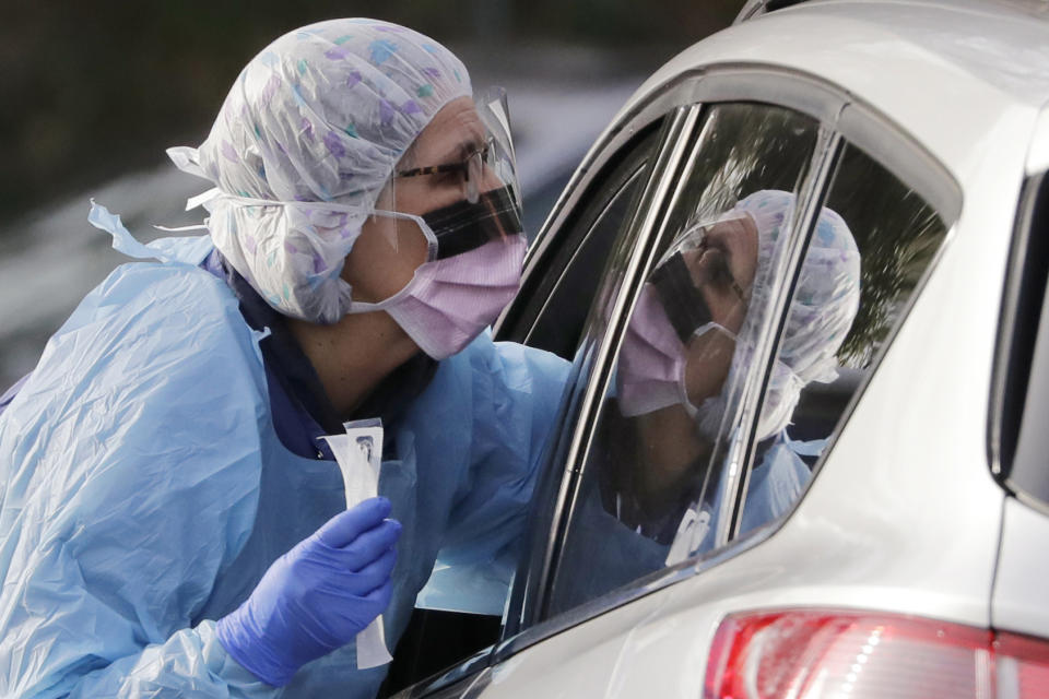 FILE - In this March 17, 2020, file photo, Laurie Kuypers, a registered nurse, reaches into a car to take a nasopharyngeal swab from a patient at a drive-through COVID-19 coronavirus testing station for University of Washington Medicine patients in Seattle. The federal government is rushing protective equipment to states for medical workers who will be on the front lines of the growing coronavirus pandemic. But at least in two states promised deliveries are falling far short of requests and even include expired items. Washington state has received at least two shipments and state health officials say they need more. (AP Photo/Elaine Thompson, File)