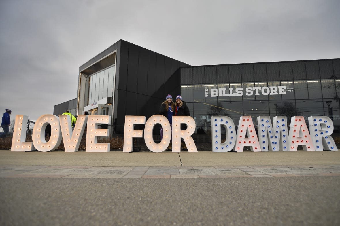 Fans stand for photographs by a sign in support of Buffalo Bills safety Damar Hamlin outside Highmark Stadium before an NFL football game against the New England Patriots, Sunday, Jan. 8, 2023, in Orchard Park, N.Y. Hamlin remains hospitalized after suffering a catastrophic on-field collapse in the team’s previous game against the Cincinnati Bengals. (AP Photo/Adrian Kraus)