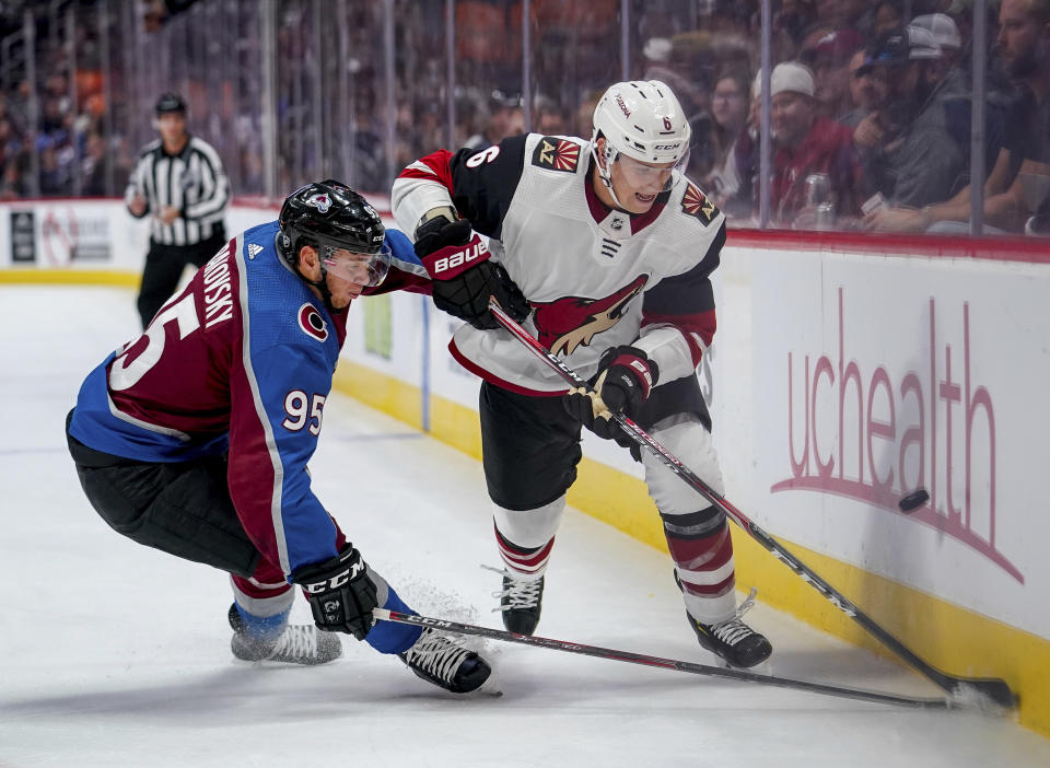 Arizona Coyotes defenseman Jakob Chychrun (6) and Colorado Avalanche left wing Andre Burakovsky (95) chase the puck along the boards during the second period of an NHL hockey game, Oct. 12, 2019, in Denver. Chychrun will play for Arizona to start the season, but has agreed to the team’s proposal to be traded to a playoff contender. (AP Photo/Jack Dempsey, file)