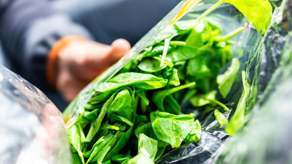 closeup of person hands holding fresh raw, plastic packaged bag of green spinach, vibrant color, healthy salad