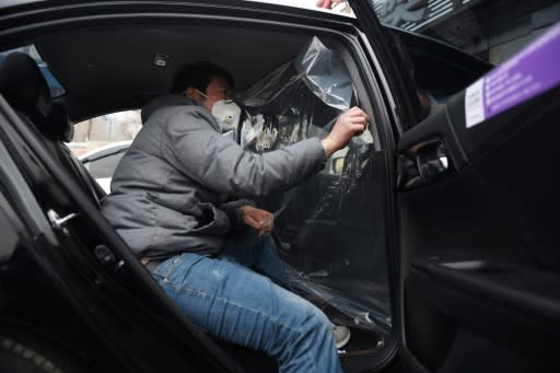 Workers install a plastic shield between the front and rear seats of a car used for ride-hailing in Beijing