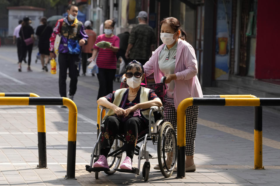 A woman in a wheelchair wearing a mask is pushed past barriers in Beijing, Tuesday, Aug. 30, 2022. (AP Photo/Ng Han Guan)