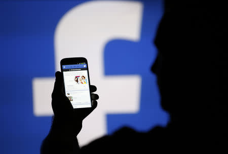 FILE PHOTO: A man is silhouetted against a video screen with an Facebook logo as he poses with an Samsung S4 smartphone in this photo illustration taken in the central Bosnian town of Zenica, August 14, 2013. REUTERS/Dado Ruvic