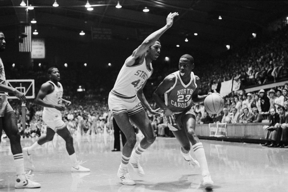 michael jordan dribbling a basketball past another player while sticking his tongue out on a basketball court