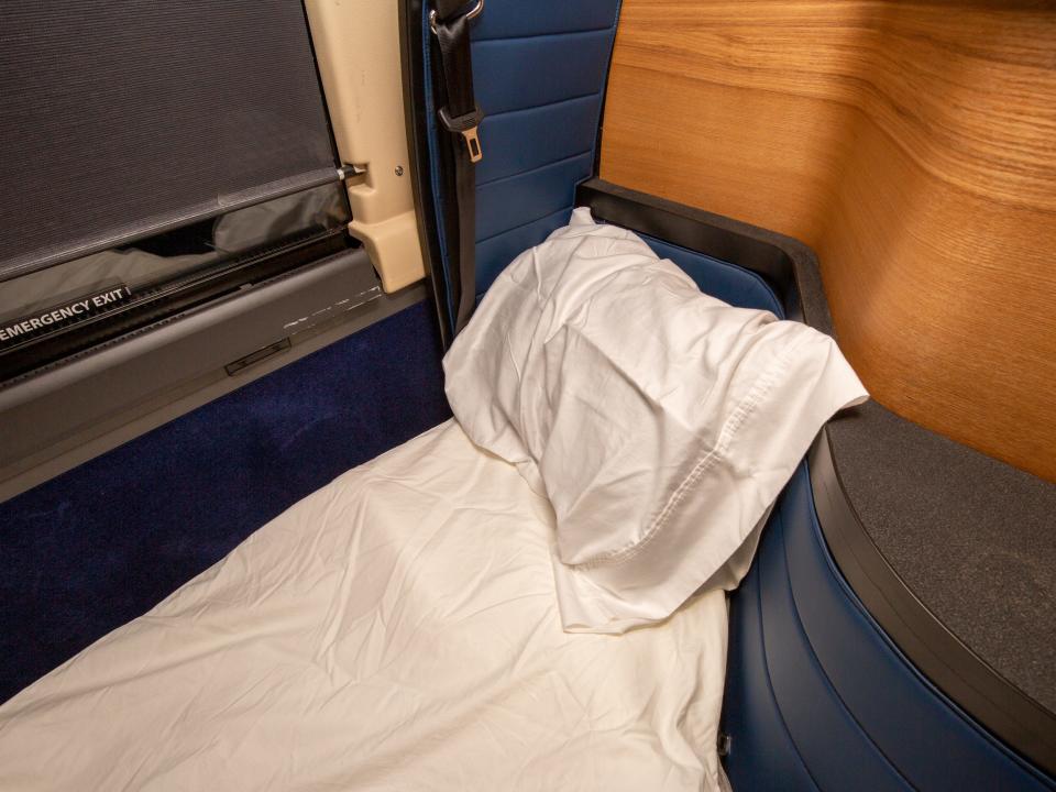 A pillow and mattress next to the window of a bus.