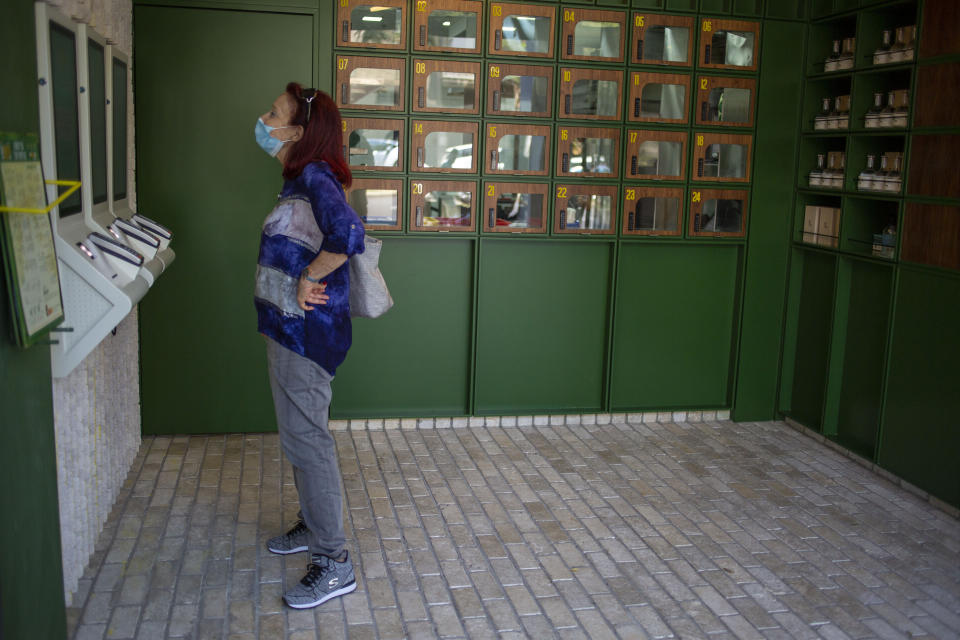 A customer reads the menu at Go noodles, where her order will be served in one of the glass-paned lockers seen behind her in Tel Aviv, Israel, Thursday, July 16, 2020. The coronavirus crisis and its economic impact have forced many small businesses and restaurants to shut their doors in recent months, but Tel Aviv's Go Noodles opened a new branch last week that features digital-only ordering and pickup from lockers. (AP Photo/Ariel Schalit)