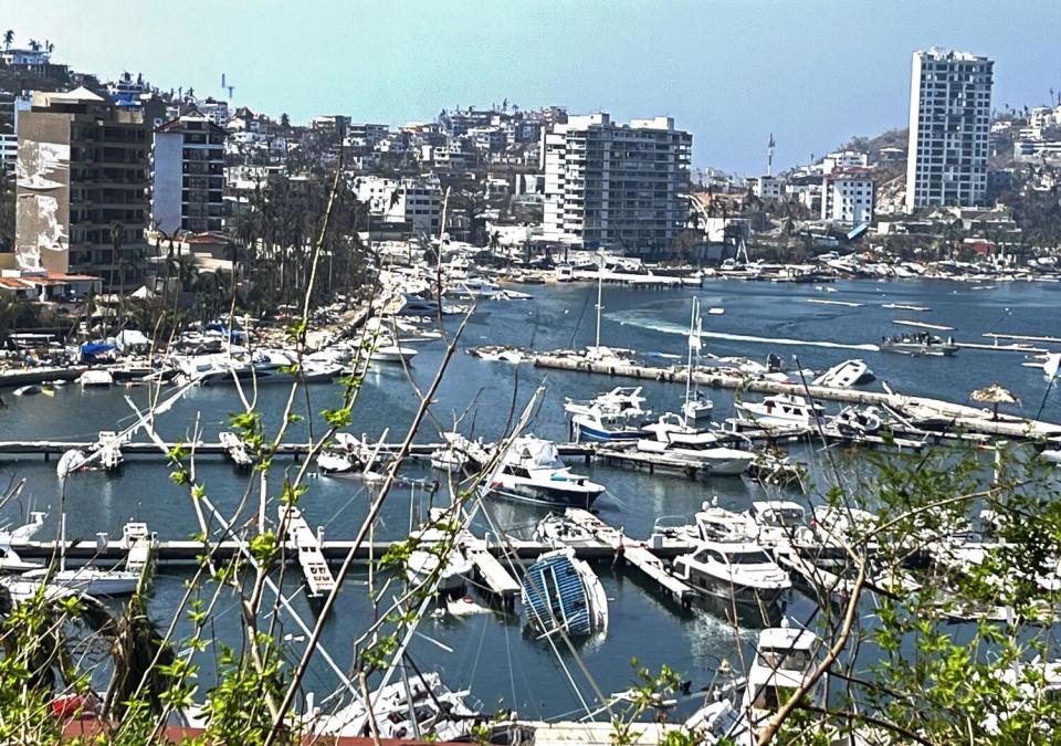 Ruined boats float in a harbor in front of shattered buildings.