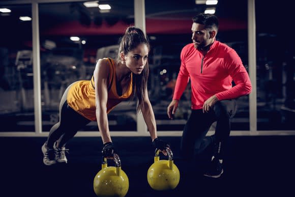 A fitness coach helping a woman train with kettlebells.